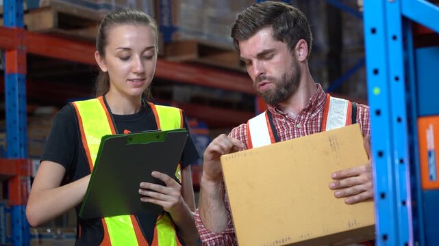 Caucasian man and woman warehouse workers talking. Man checking box he is holding while woman holds clipboard. Professional logistics team inspecting package in industrial distribution center.