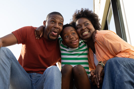 African American family with child crouching on steps leaning in making playful faces wearing watch
