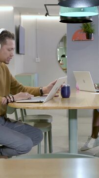 Vertical video: Heeding phone buzz man in sweater donning headset to focus typing on laptop at desk