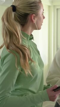 Vertical video: Turning woman in green top noticing friend arriving and showing phone at home
