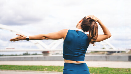 Rear view of a fit woman performing a warm-up stretch outdoors in urban environment.