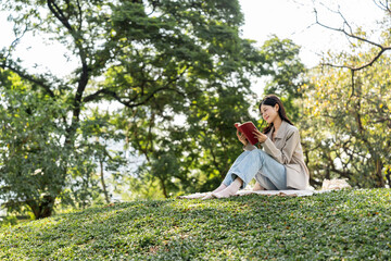 Young asian woman relaxing reading book sitting at public park life style outdoor. Happy female Take a break enjoy time living in the nature. Human and nature together