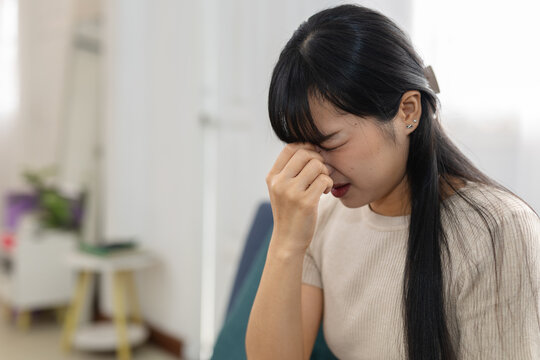 women suffering from eye strain and headache at home, pinching nose bridge with closed eyes. Stress, fatigue, sinus pain, migraine and health problem concept.