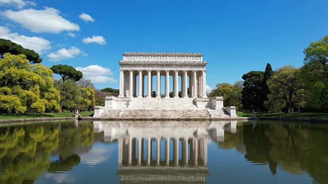 Temple of asclepius in rome italy with reflection and clear blue sky surrounded by lush green trees in villa borghese park