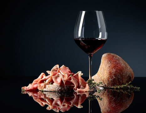 Prosciutto with ciabatta, red wine and thyme on a black background.