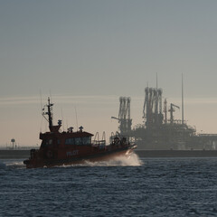 Fototapeta premium MARITIME TRANSPORT - A pilot boat sails against the backdrop of a gas terminal
