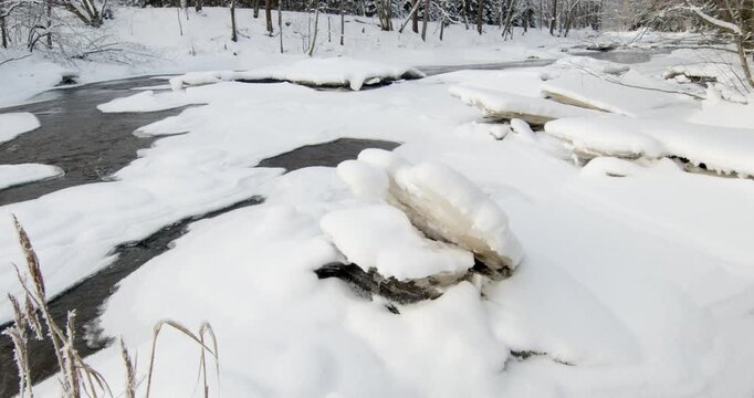 Tranquil, partially frozen river flowing through a snow-covered forest during winter, Matarinkoski, Vantaa, Finland, Europe.