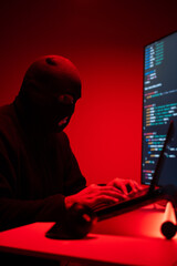 Hacker in balaclava with an obscured face is stealing data, representing cybercrime, hacking, dark web activity, and online security threats. Cyber Security concept.