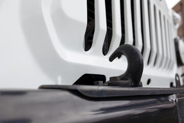  Close-up of a heavy-duty black metal tow hook on the front bumper of a white off-road vehicle.  Steel towing hook on a 4x4 car, selective focus and blurred background. © alan