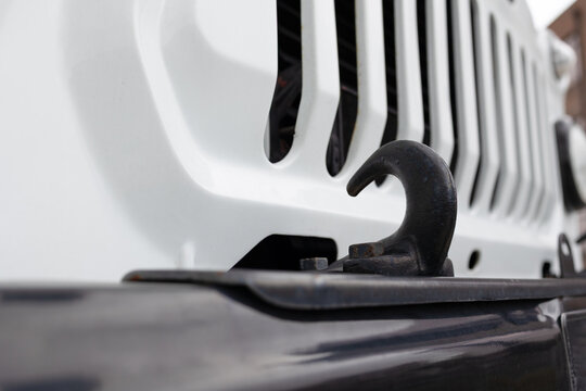  Close-up of a heavy-duty black metal tow hook on the front bumper of a white off-road vehicle.  Steel towing hook on a 4x4 car, selective focus and blurred background.