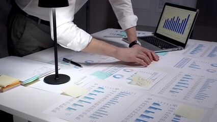 Business professional studies financial reports and market data at a cluttered desk, surrounded by...