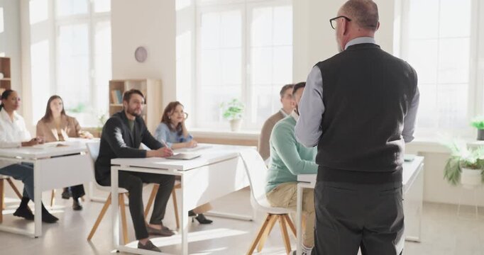 Teacher leads students classroom training lecture workshop. Adults take notes as the teacher gives coaching, leading discussion and learning in a bright room. Concept shows teamwork and study.