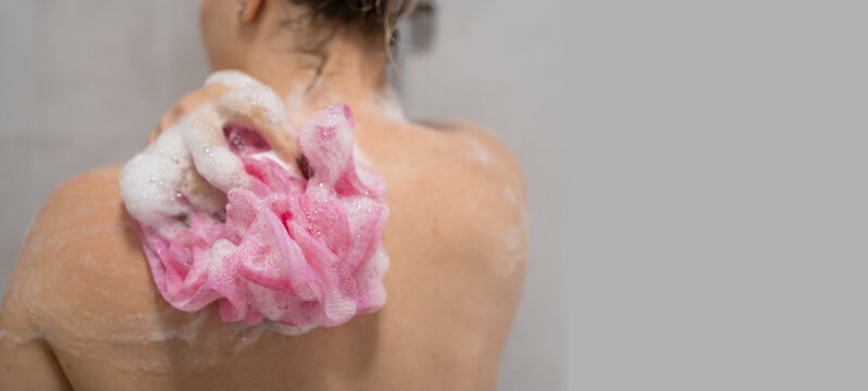 Woman washing with sponge and shower gel foam. scrubbing skin in bathroom. hygiene, skincare and wellness routine