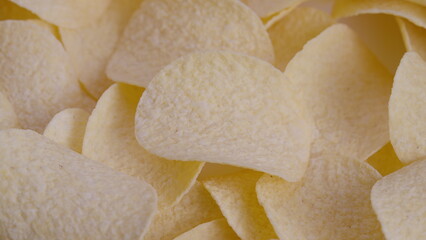 Close up potato chips pile revealing crispy curved crisps, soft beige tones, light grainy surface,...
