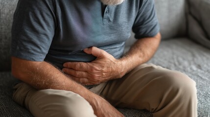 Mature man sitting on sofa holding his stomach in pain