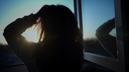 brunette woman stands on the balcony at sunset and looks out the window, touches her hair, have fun and enjoy © vla