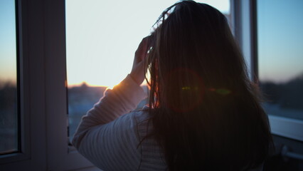woman stands on the balcony at sunset and looks out the window, touches her hair, have fun and enjoy © vla