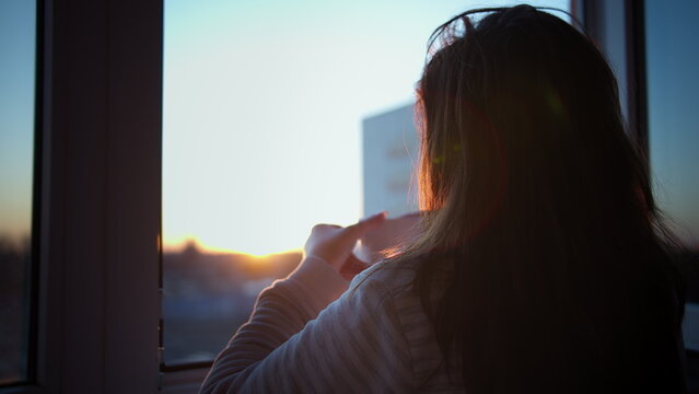 pretty brunette woman drinking coffee on the balcony at sunset, back view, have fun and enjoy