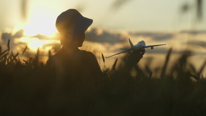 funny boy playing with airplane in the golden wheat field at sunset, boy dreams of being a pilot, sunset light © vla
