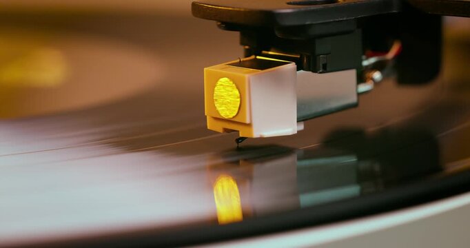 Detailed close-up of a turntable tonearm with white cartridge headshell, positioned over a black vinyl record on the platter, highlighting audio equipment precision.