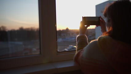 happy woman stands on the balcony and photographs the sunset on her phone, have fun, have fun and enjoy © vla
