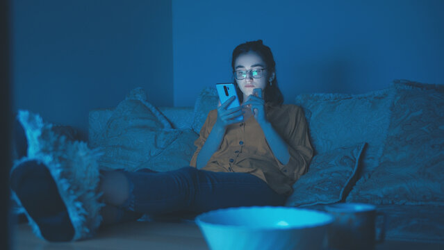 Girl Sitting on Sofa at Night Using Smartphone with Feet on Table, have fun and enjoy