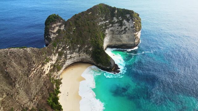 Aerial drone view of the iconic T-Rex cliff formation at Kelingking Beach, Nusa Penida, Bali. Steep limestone cliffs drop into the deep blue Indian Ocean, with waves crashing against the secluded beac