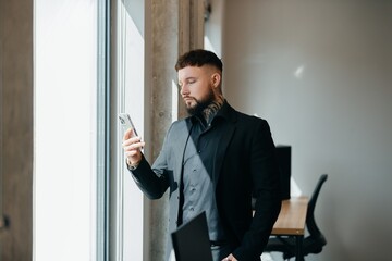 Fototapeta premium Tattooed businessman using smartphone in modern workspace
