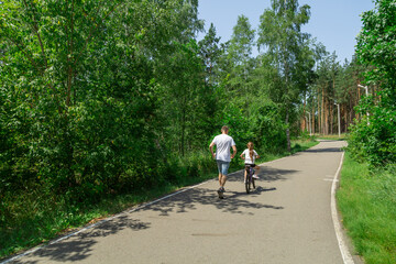 Fototapeta premium Dad teaches daughter to ride a bike. Girl sat on bicycle for the first time, his father teaches child to ride a bicycle.