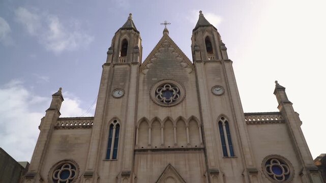 Neo-gothic towers of the Carmelite Balluta Parish Church in Saint Julian's, Malta seen from low angle, dramatic clouds moving across the sky above the twin spires.