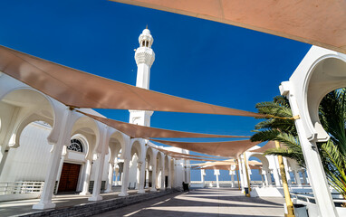 Exterior view of the Al Rahmah Mosque in Jeddah featuring traditional white arches and modern sunshades under a bright blue sky.