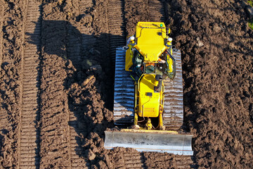 Yellow bulldozer works on field soil during sunny day in rural area with clear blue sky © Iryna
