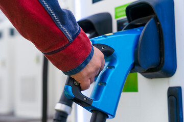 Charging an electric vehicle at a charging station in a busy urban area during daylight hours © Iryna