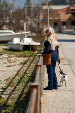 Woman with her dog Jack Russell on a leash visits a seaside village in Sicily. The woman is seventy years old and has long blond hair