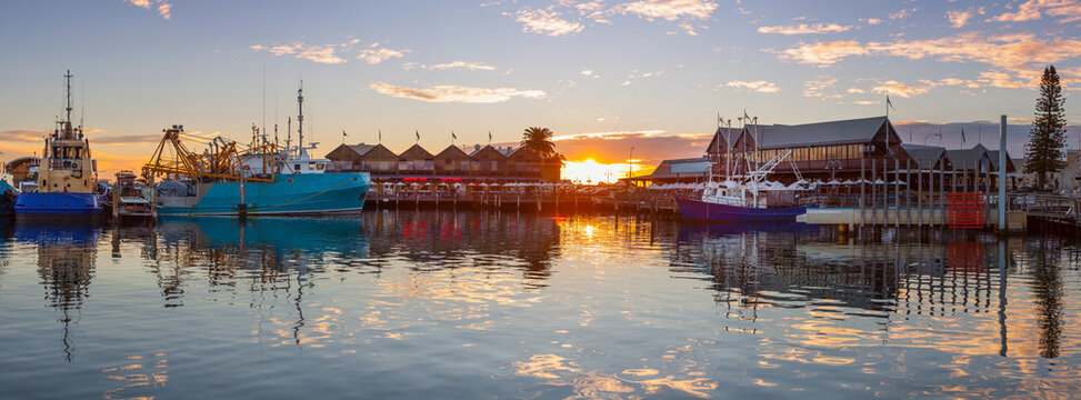 Panoramic view of sunset over fishing fleet and buildings reflecting on the waters of a marina