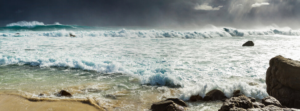 Low angled view of a black stormy sky over rough waves breaking over shoreline rocks