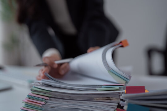 Businesswoman's hands with a pen flipping pages through a tall stack of file folders with colorful tabs on a minimalist desk, conveying organization, workload and deadlines