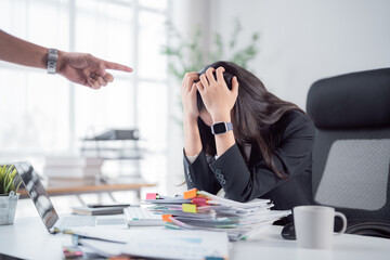 Obraz premium Frustrated employee facing pressure and blame from a pointing boss, feeling overwhelmed by workload and stress while working at her office desk surrounded by documents