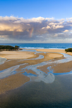 Aerial view of an inland lake flowing out to sea under a colourful cloud formation and rainbow