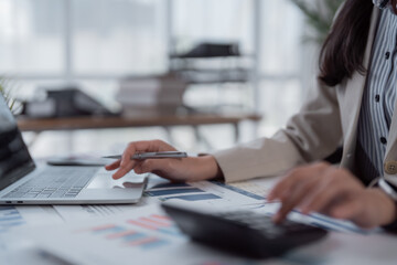 Fototapeta premium Businesswoman's hands are busy calculating financial data, analyzing reports, and typing on a laptop, emphasizing efficiency and accuracy in bookkeeping, accounting, and corporate strategy