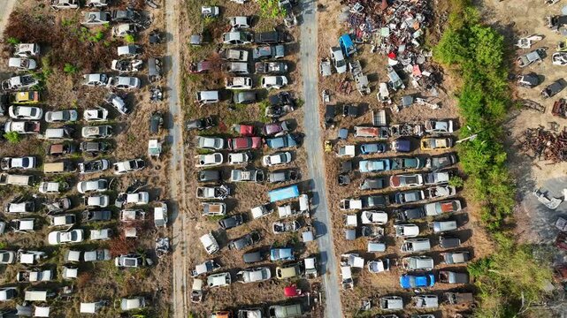 Drone aerial perspective of a massive junk car yard with rows of damaged vehicles and scrap piles, representing vehicle disposal systems, recycling operations, and industrial waste management.
