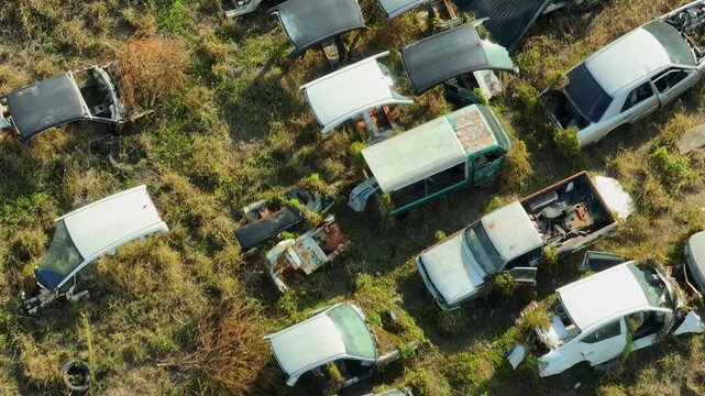 Drone aerial close perspective of rows of abandoned and wrecked cars in a junkyard, highlighting vehicle dismantling, scrap metal recovery, and the lifecycle of aging automobiles.
