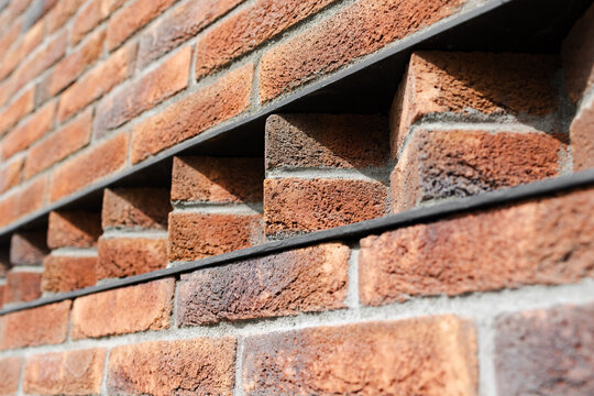 Contemporary clinker brickwork featuring decorative openings and unique architectural texture.  Modern red brick wall with creative recessed patterns and shadow play.