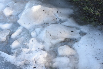 Obraz premium Horizontal photo of spring ice remnants partially bordering grass. Transition from ice to greenery.