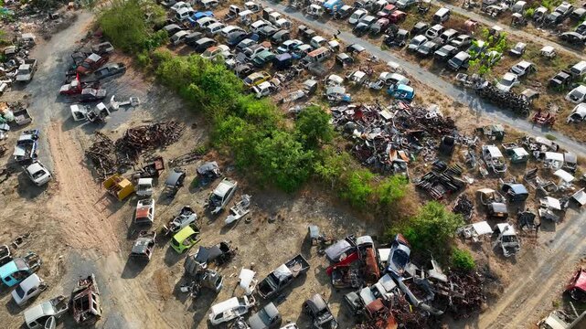 Top-down drone image of a massive car graveyard with rusting vehicles scattered across dirt lanes, representing auto recycling, end-of-life vehicles, and industrial scrap processing.
