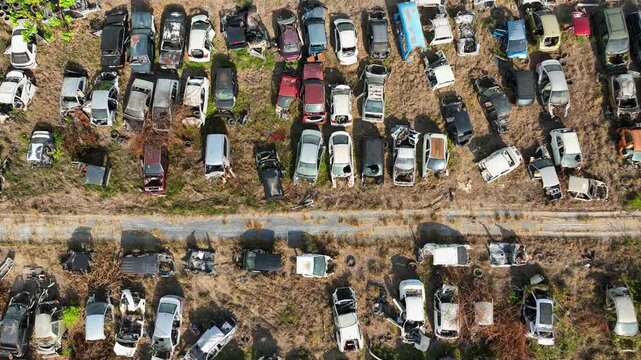 Aerial drone view of a scrapyard filled with hundreds of old and damaged cars arranged along dirt lanes, illustrating abandoned vehicles, accident aftermath, and the lifecycle of aging automobiles.
