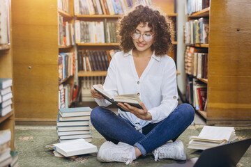 Young woman learning and studying in library, reading book, surrounded by bookshelves and texts, engaging in research © anatoliycherkas