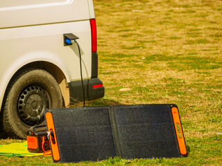 Solar panel system charging battery for van on grass field during daytime © Voyagerix