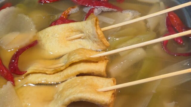 Close-up of Korean fish cakes (Eomuk-tang) on wooden skewers simmering in a savory broth with red chili peppers and radish.