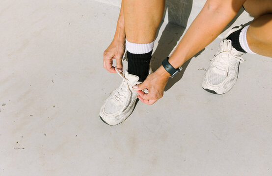 Tying shoelaces of white sneakers on a sunny day